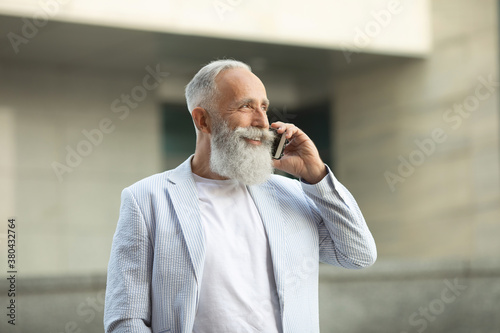 Excited old man in jacket with white hair and beard talking on phone.