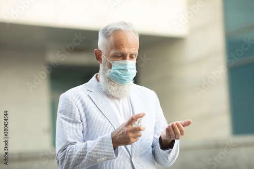 Coronavirus. Cleaning hands with sanitizer spray in city. Bearded senior man wearing in medical protective mask on street. Sanitizer to prevent Coronavirus, Covid-19, flu.Virus and illness protection.