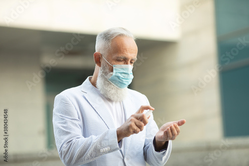 Coronavirus bearded senior man wearing face mask using antiseptic bottle dispenser hand sanitizer alcohol gel hand wash. Covid-19.