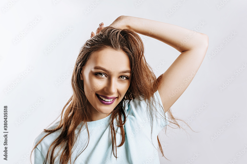 Beautiful sweet brunette girl with long hair with fashion makeup with purple lips on an isolated gray background. The woman holds her hand to her face and looks into the camera. Kind cute model Beautiful sweet brunette girl with long hair with fashion makeup with purple lips on an isolated gray background. The woman holds her hand to her face and looks into the camera. Kind cute model