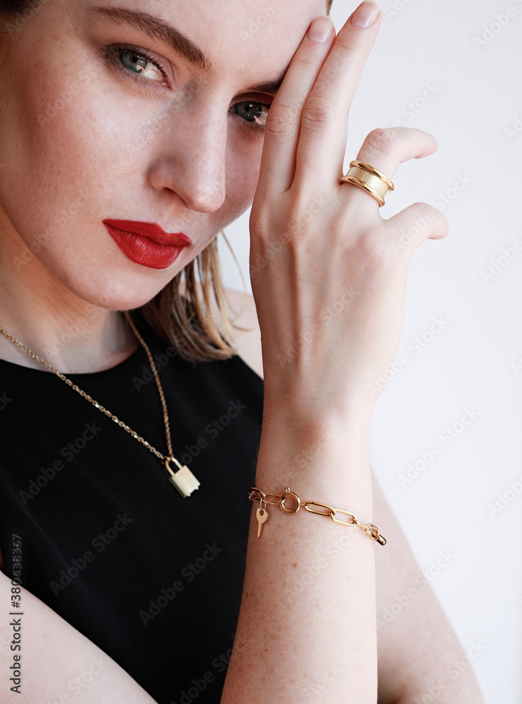 Close-up portrait of beautiful woman with red lips and golden jewellery posing over white wall background. Vertical.