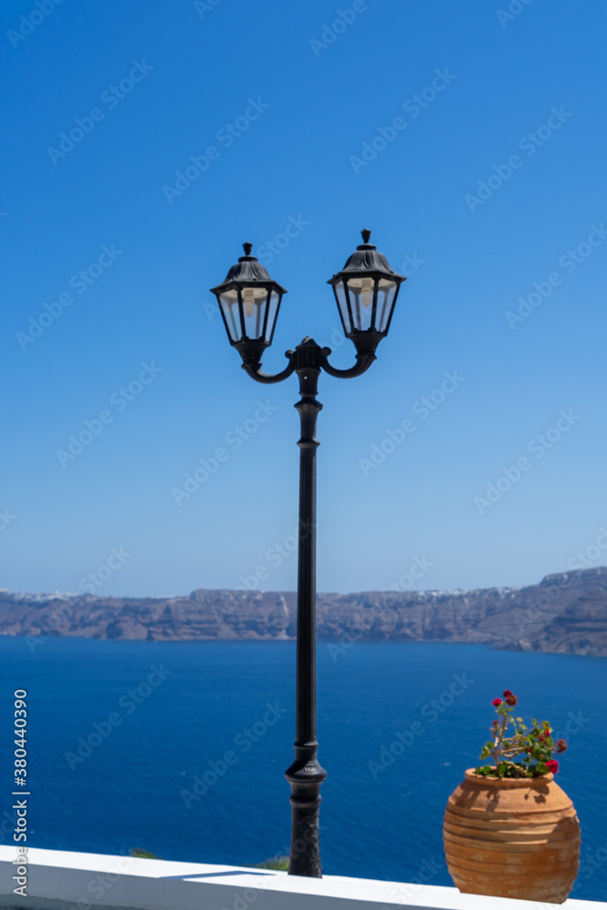 Vintage lantern and terracotta flower pot against blue sky scenic view to caldera of Santorini,Cyclades, Greece