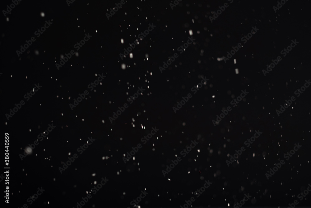 Snow background. Defocused white flying dust isolated on black surface. Dark sky. Winter holidays night. Blur powder pattern New Year abstract wallpaper.