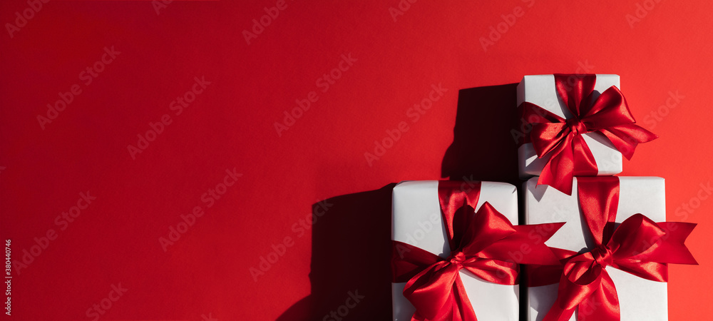 Festive background. Christmas surprise. Pile of wrapped white gift boxes with ribbon bows isolated on red empty space party invitation card. New Year decoration. Festive background. Christmas surprise. Pile of wrapped white gift boxes with ribbon bows isolated on red empty space party invitation card. New Year decoration.