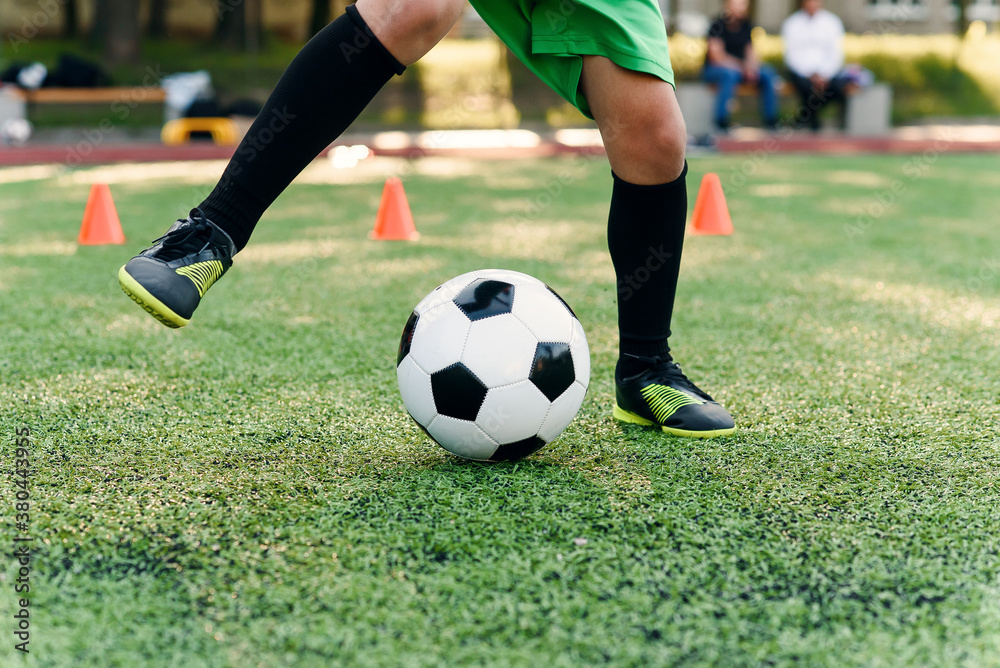 Persistent teen soccer player kicking ball on field. Close up feet of footballer kicking ball on green grass.