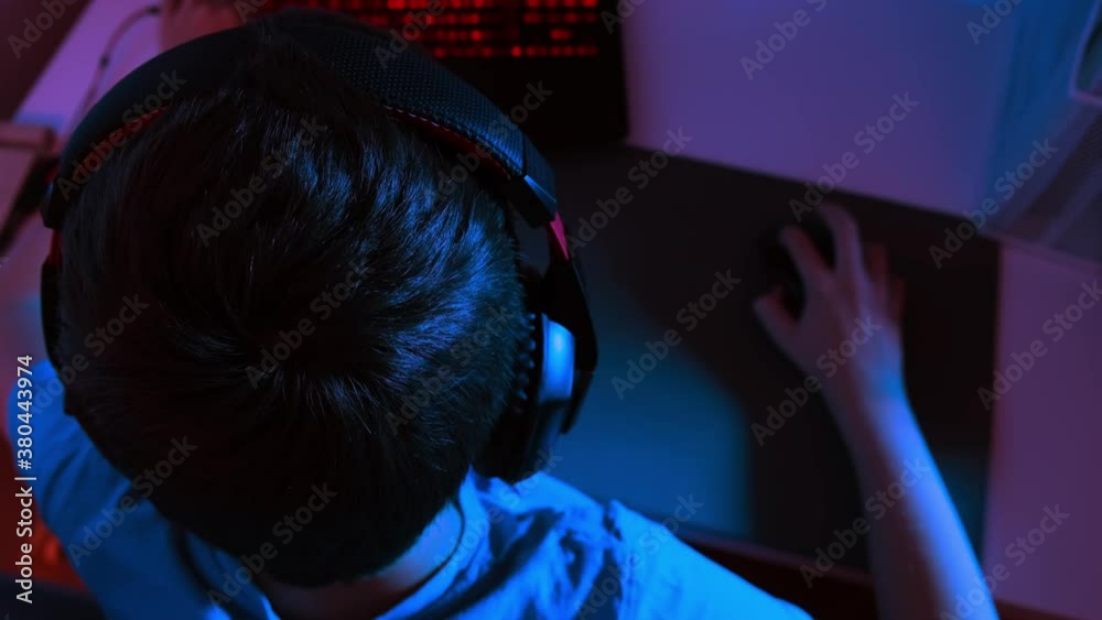 A boy in headphones playing online computer game at night, he is immersed in atmosphere of virtual reality A boy in headphones playing online computer game at night, he is immersed in atmosphere of virtual reality