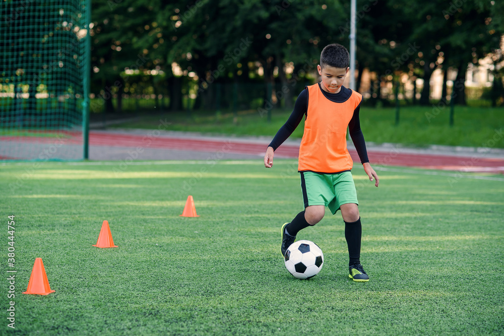Obraz premium Soccer player kicking ball on field. Soccer players on training session. Teen footballer kicking ball on green grass.