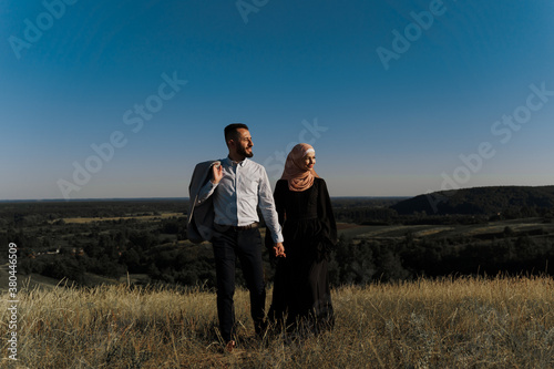 Muslim love story on the blue sky background. cheerful mixed couple smiles and hugs . Woman weared in hijab looks to her man. Advert for on-line dating agency © Rabizo Anatolii