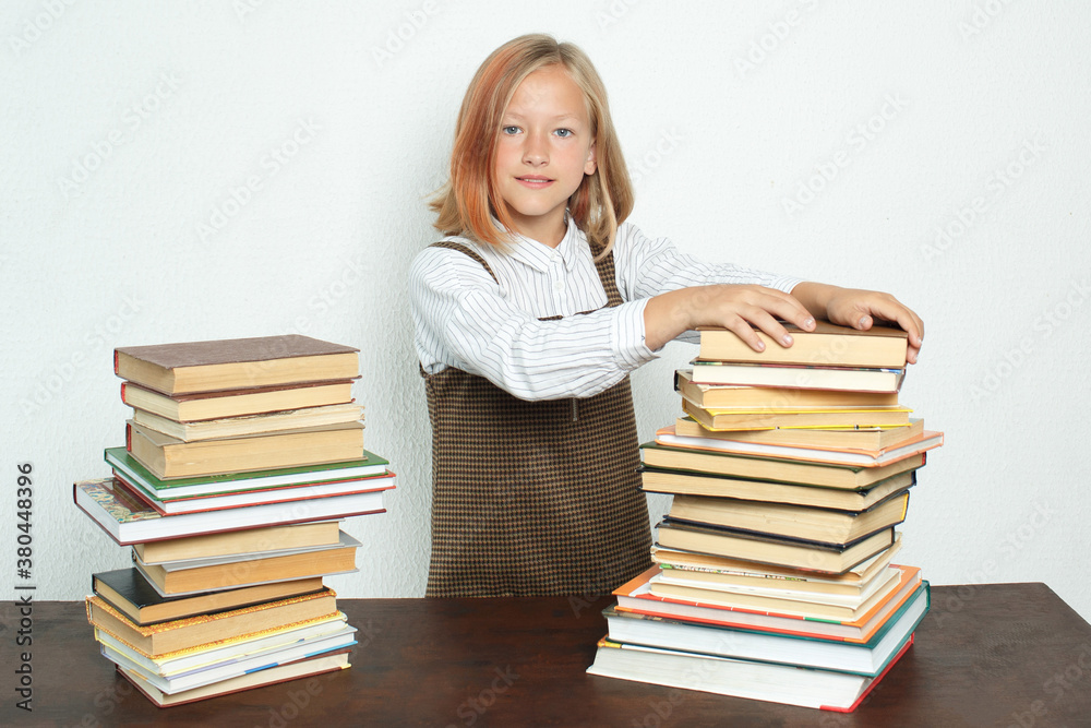 A teenage girl takes books from a stack of books on the table. A teenage girl takes books from a stack of books on the table.