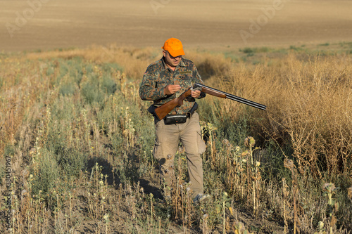 Duck hunter with shotgun walking through a meadow.