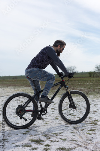 Sports brutal bearded guy on a modern mountain bike. A cyclist in a salt deserted place by the lake.