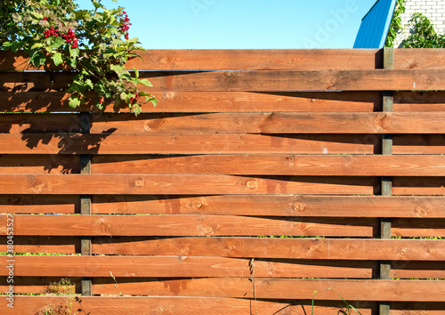 brown fence made of wooden curved boards and viburnum bush