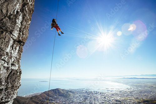 mountaineer abseiling next to a sheer cliff overlooking a city photo