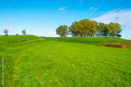 Dike in a green grassy field in sunlight under a blue sky in autumn, Almere, Flevoland, The Netherlands, September 24, 2020 
