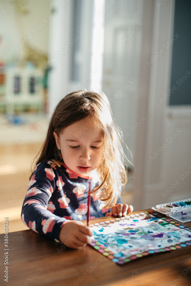 Cute young girl painting watercolors on a dining room table Cute young girl painting watercolors on a dining room table