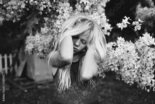 portrait of blonde girl in black and white moody next to flowering tree photo