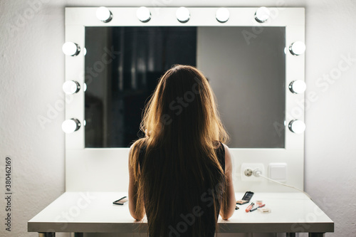 Vew from behind of a woman making her face in a dressing room