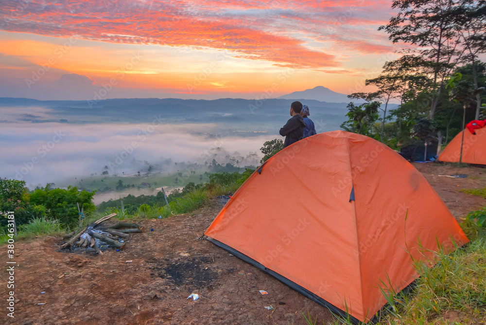 Camping on the mountain peak with tend. Watching beautiful sunrise over the clouds. Perfect for adventure and traveling concept. 