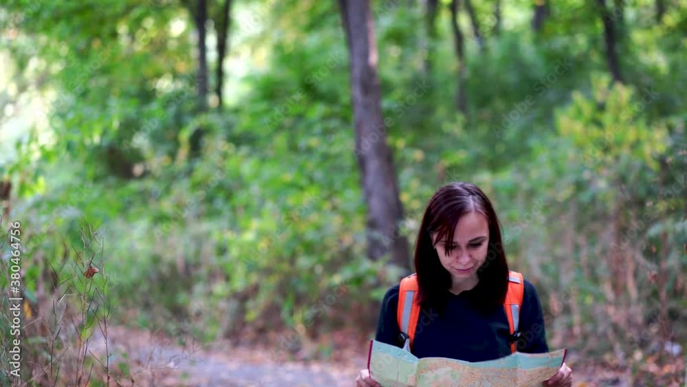 Traveling woman with map in woods. Woman with backpack walking in woods. Female carrying backpack and walking in sunny autumn forest