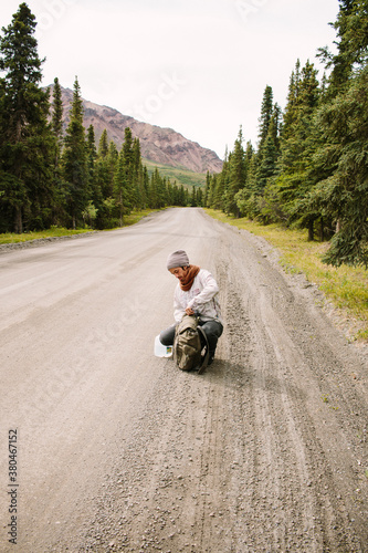 Young Man Rummaging Through His Backpack On A Gravel Road In Denali National Park