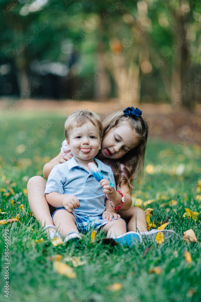Sister and brother sitting in grass sharing a popsicle Sister and brother sitting in grass sharing a popsicle