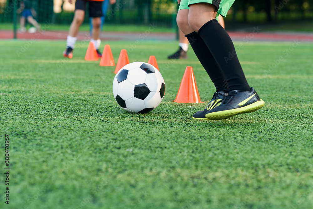 Persistent teen boy in sportswear trains football on soccer field and learns to circle the ball between training cones. Persistent teen boy in sportswear trains football on soccer field and learns to circle the ball between training cones.