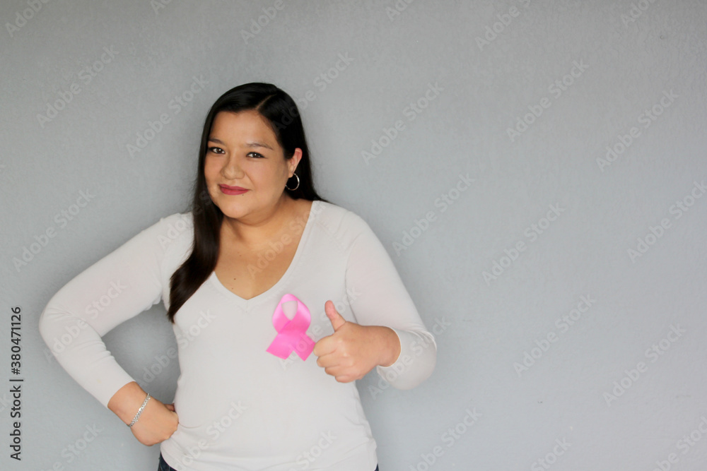 Latin woman with pink ribbon in hands and plain gray background for campaign against breast cancer Latin woman with pink ribbon in hands and plain gray background for campaign against breast cancer