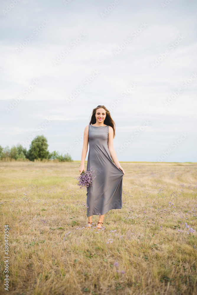 Beautiful young woman standing in a field and holding flower bouquet Beautiful young woman standing in a field and holding flower bouquet