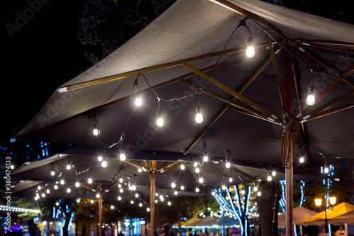 textile umbrella with a wooden frame and edison pendant lamps glowing with light on a backyard terrace night scene, nobody.