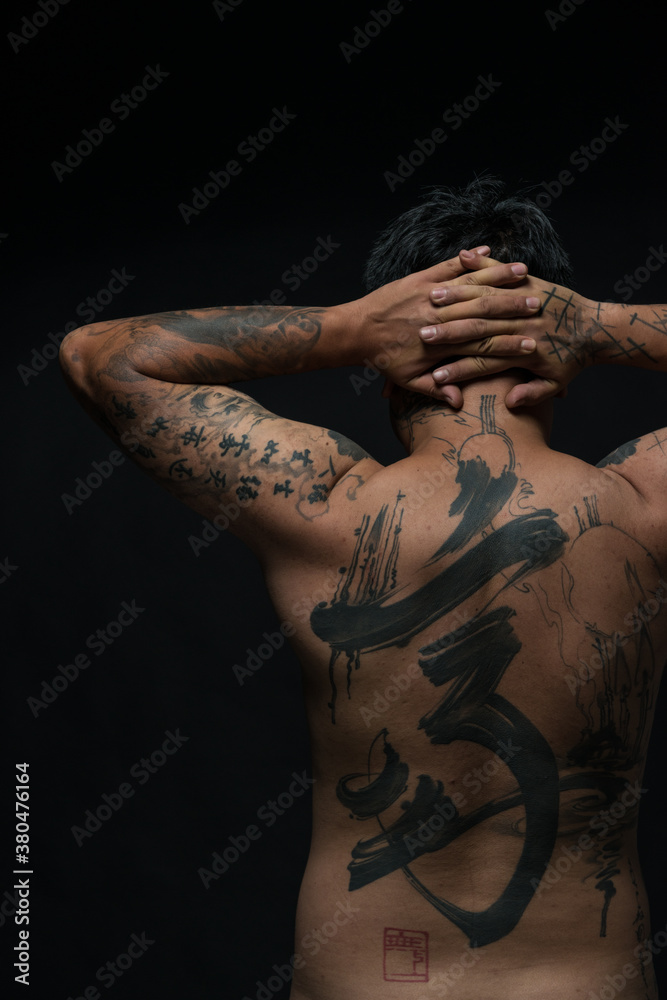 Rear view studio shot of tattooed young man with hands behind head