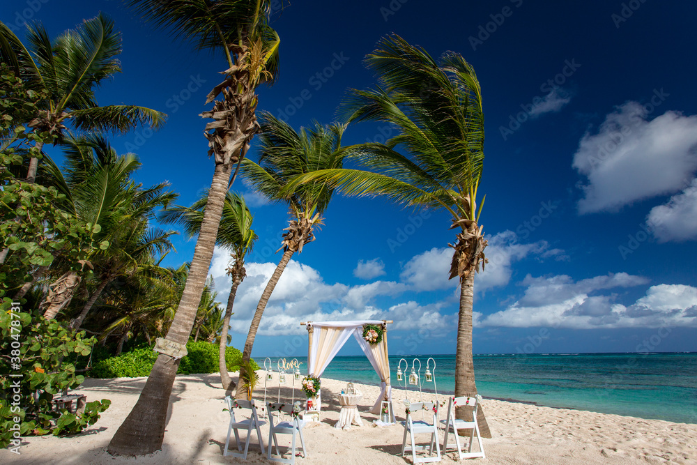 Wedding bamboo gazebo, decorated with tropical flowers and coloured fabrics on the paradise beach with palm trees, white sand and blue water of Caribbean Sea, Punta Cana, Dominican Republic 