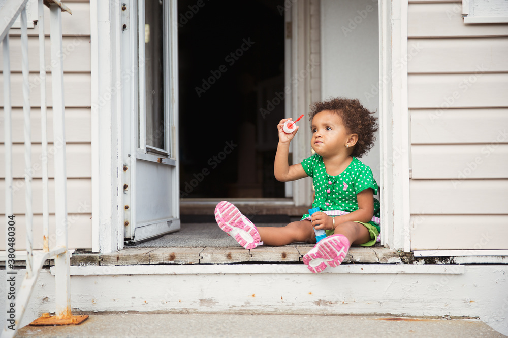 Toddler sitting happily with bubble blower at the entrance of an old wooden house Toddler sitting happily with bubble blower at the entrance of an old wooden house