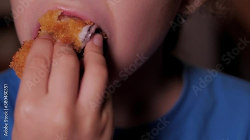 Child on a brown background is eating eating fast food, nagins, breaded colmar. Portrait Close up kid or little girl eats food, chicken nuggets, wings and french fries.Concept woman of puffy lips eat photo