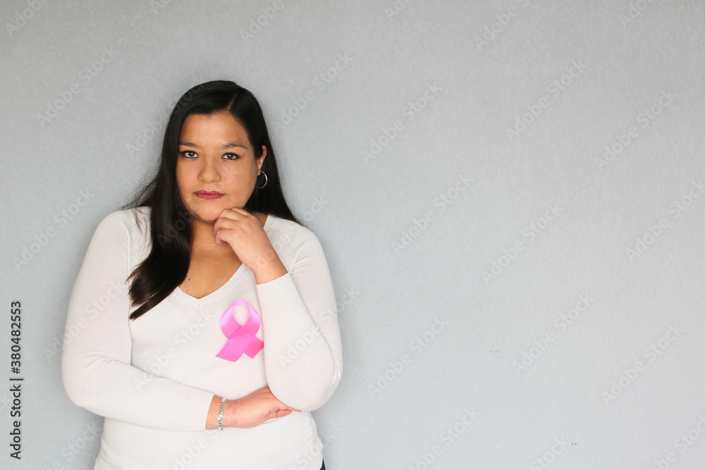 Latin woman with pink ribbon in hands and plain gray background for campaign against breast cancer Latin woman with pink ribbon in hands and plain gray background for campaign against breast cancer