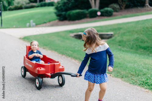 Cute big sister pulling her baby brother in a wagon