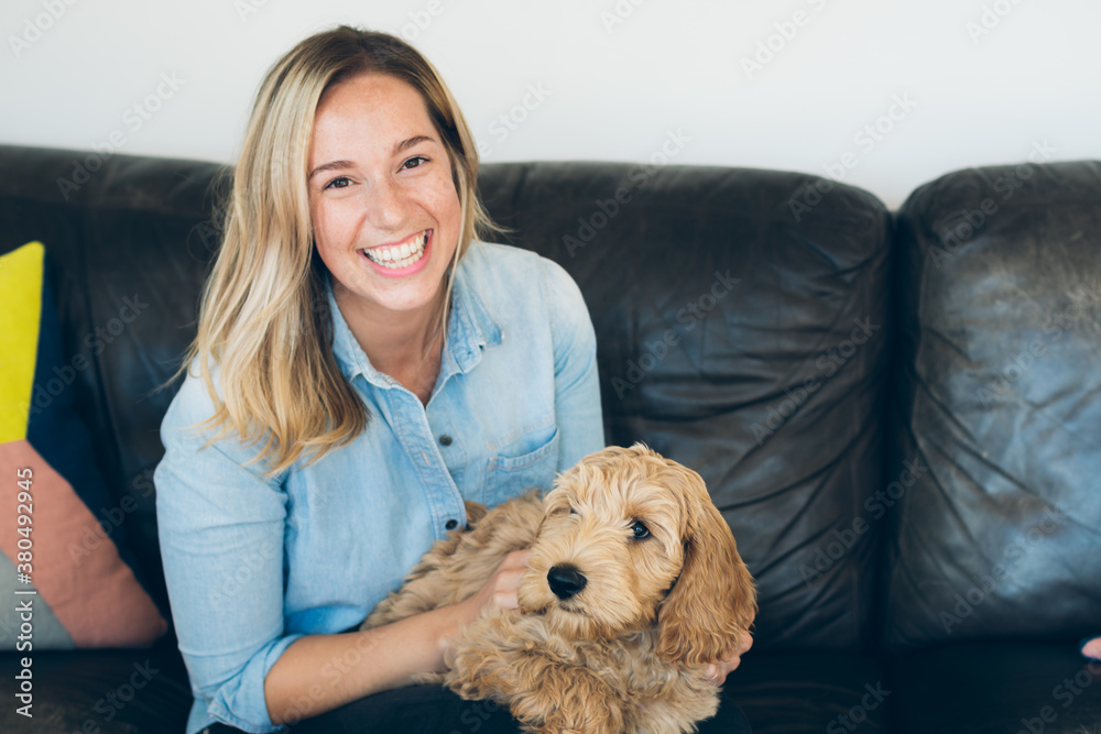 Happy Young Woman Sitting On Couch Holding And Petting Labradoodle Puppy Happy Young Woman Sitting On Couch Holding And Petting Labradoodle Puppy