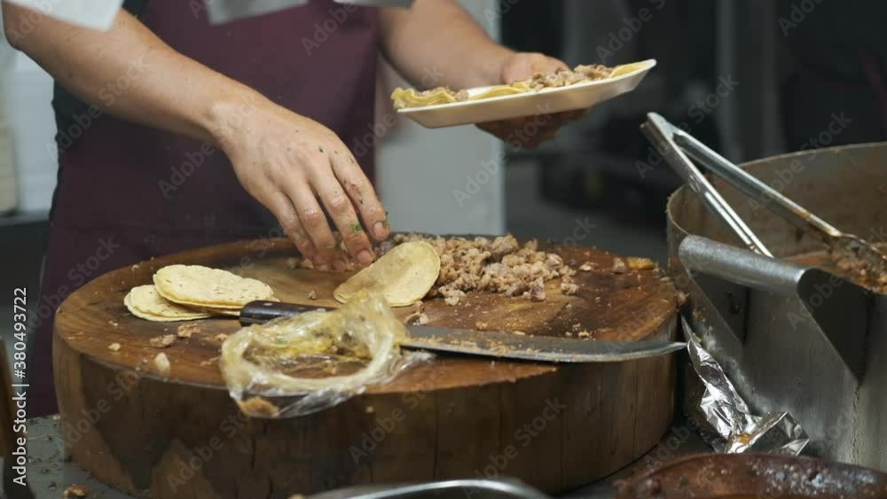 A man is putting tacos on a plate in a mexican street food restaurant