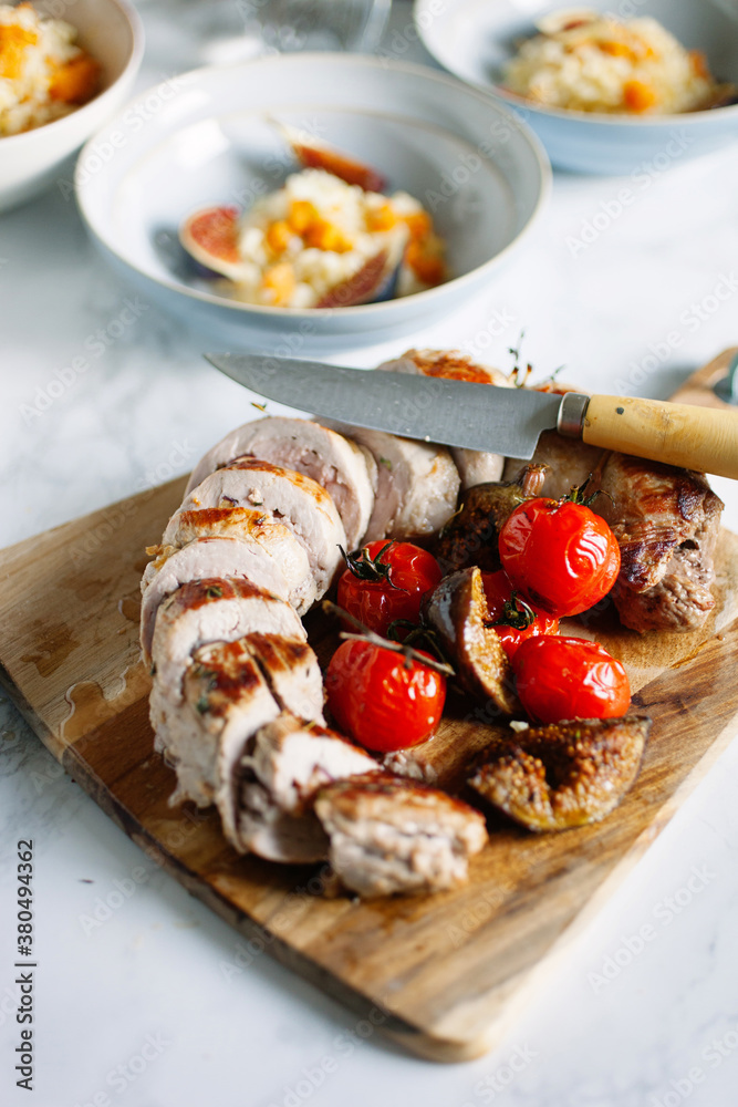 Roast pork fillet/tenderloin with figs and tomato on a cutting board.