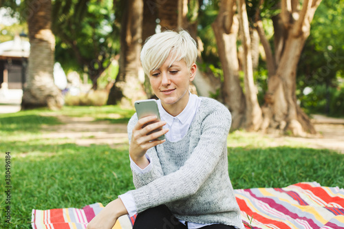 Blonde woman texting on her phone in the park.