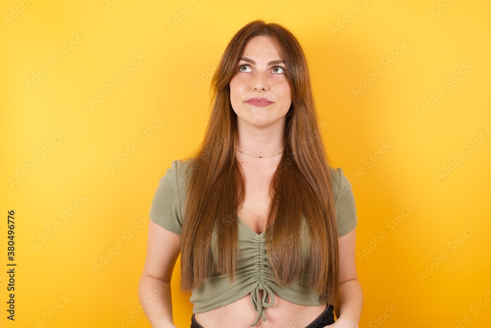 Obraz premium Young caucasian woman with long hair wearing green tshirt standing over isolated yellow background, looking aside into empty space thoughtful isolated over yellow background
