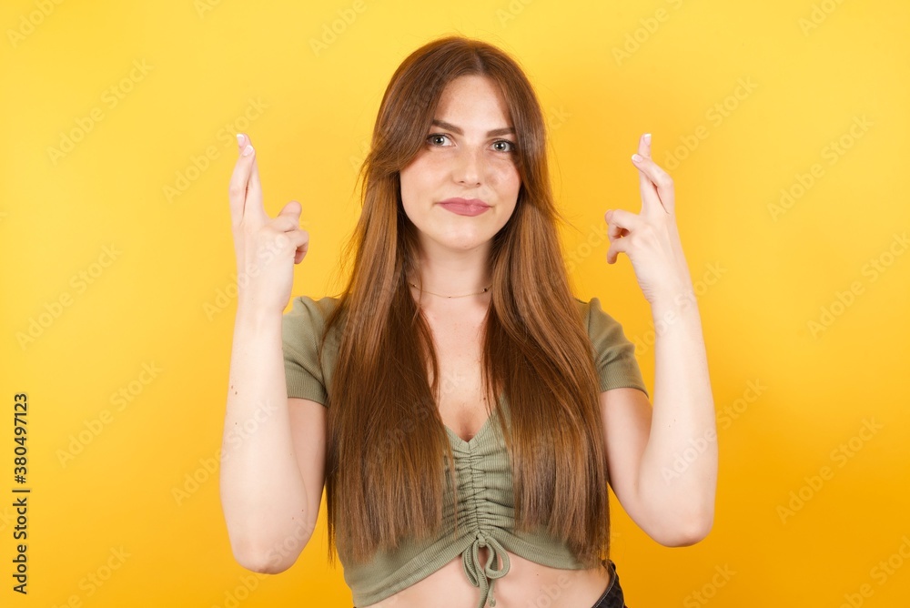 Young caucasian woman with long hair wearing green tshirt standing over isolated yellow background showing rock and roll hand gesture Young caucasian woman with long hair wearing green tshirt standing over isolated yellow background showing rock and roll hand gesture