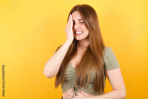 Young caucasian woman with long hair wearing green tshirt standing over isolated yellow background Yawning tired covering half face, eye and mouth with hand. Face hurts in pain.