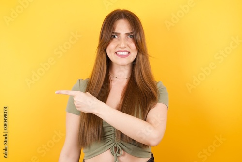 Young caucasian girl wearing sexy t-shirt over isolated yellow background Pointing aside worried and nervous with forefinger, concern and surprise concept.