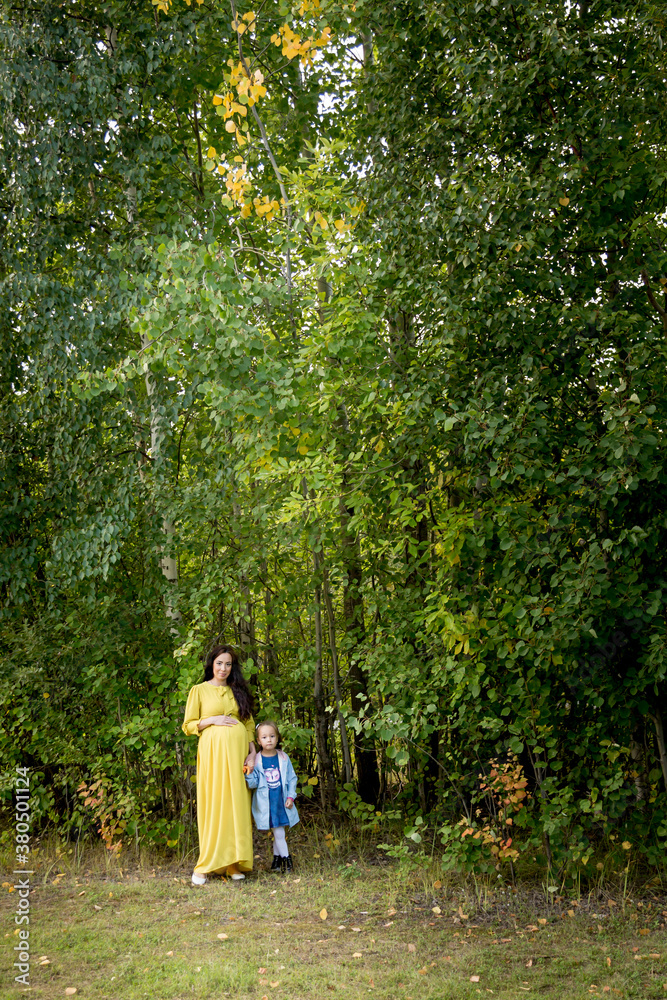 Pregnant woman in yellow dress with her daughter in nature Pregnant woman in yellow dress with her daughter in nature