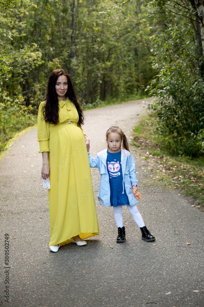 Pregnant woman in yellow dress with her daughter in nature Pregnant woman in yellow dress with her daughter in nature