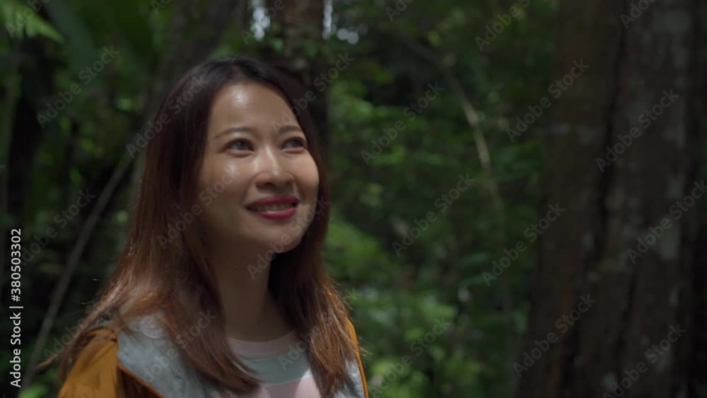 4K Smiling young beautiful Asian woman tourist in yellow jacket walking alone on forest footpath. Pretty girl hiker enjoy hiking in beautiful nature. Outdoor lifestyle and travel vacation concept. 4K Smiling young beautiful Asian woman tourist in yellow jacket walking alone on forest footpath. Pretty girl hiker enjoy hiking in beautiful nature. Outdoor lifestyle and travel vacation concept.