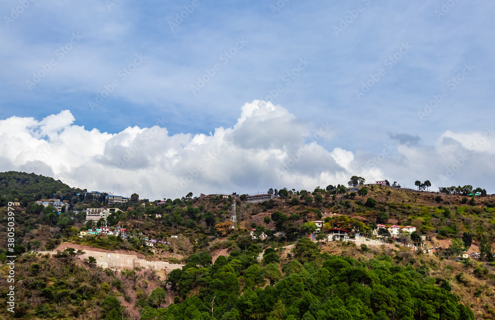 wide view of a mountain with residential properties shot from low angle and clouds in the blue sky