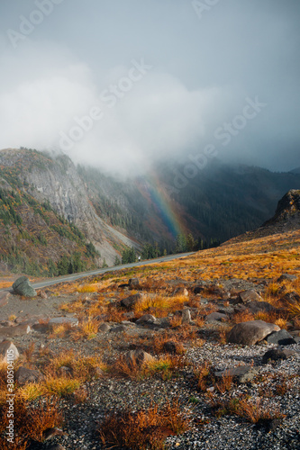 Rainbow And Dark Clouds Over Rocky Mountainside