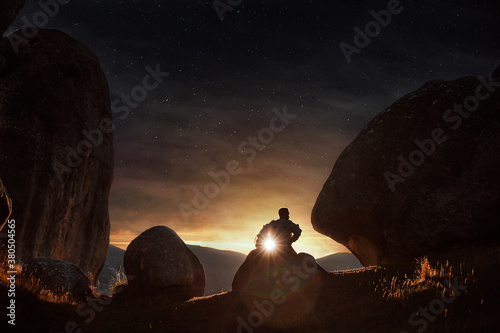 A young astronaut sits and ponders under the setting sun as a starry night emerges above him. photo