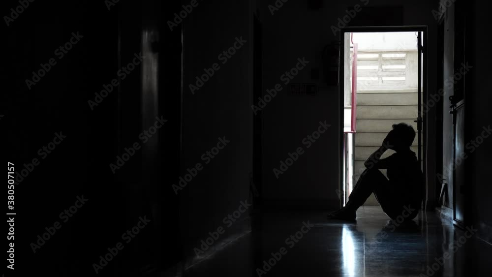 Silhouette of a sad man sitting in the dark leaning against the wall in old condo, Domestic violence, family problems, Stress, violence, The concept of depression and suicide